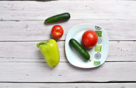 still life with tomatoes, cucumbers, pepper and plate with ornament isolated on an old wooden light rustic tableの写真素材