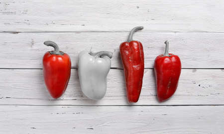 top view of three red and one monochrome peppers arranged in a row on old rustic white wooden table, copy spaceの写真素材