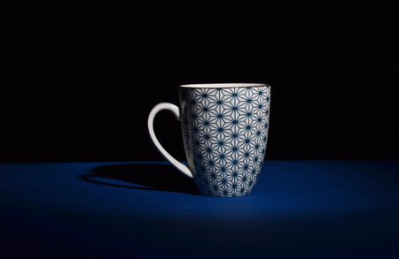 white ceramic cup with blue ornament in the darkness on blue desk and isolated on black background, copy spaceの写真素材