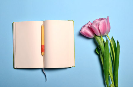 Flat lay with open book with empty pages, pen and pink tulips for invitation or congratulations on...
