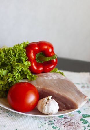 A piece of raw pork on a white plate with lettuce, tomato, garlic and sweet pepper. Healthy eating and cooking at home conceptの写真素材