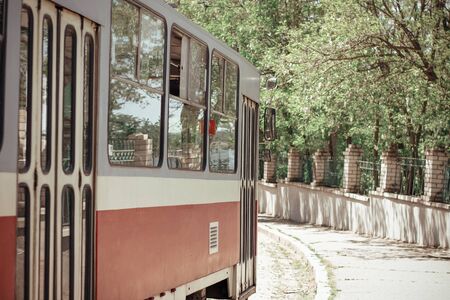 Tram in the sunny  city near a stone fence with green trees. Close viewの写真素材