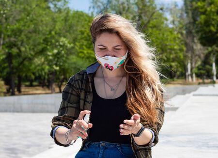Young blonde girl in white protective medical mask with fish is spaying blue sanitizer.の写真素材