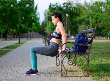 Beautiful  brunette is pushing  up from the wooden bench  in the park. Concept of sport and wellness の写真素材