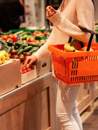 Girl picking up a branch of tomatoes  and holds an orange basket  full of fruits in her left hand in a supermarket
の写真素材