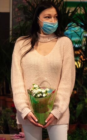 Girl dressed  in a light sweater holds a flowerpot with white flowers in a shopの写真素材