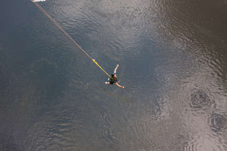 Concept of Extreme Sports and Fun. A man is a  thrill-seeker and a  rope jumper from the bridge. He is very happy to make a dream come true. He  is holding an action camera and insanely happyの写真素材