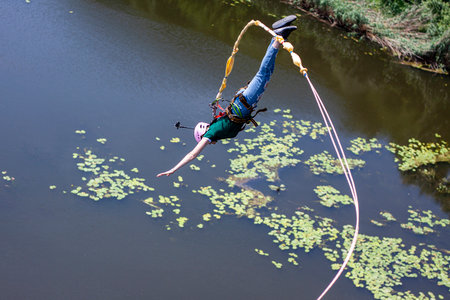 Ivanovsky Bridge, Ukraine - June 21, 2020: Concept of Extreme Sport. A girl is  doing rope jumping from the bridge. She is very happy to make a dream come true. She is holding an action cameraのeditorial素材