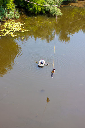 Ivanovsky Bridge, Ukraine - June 21, 2020: a man in a boat is trying to catch a man hanging on a...
