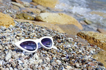 White female glasses called "cat's eye" on the stones, pebbles and sand by the sea water. Leisure and vacation concept. Fashion style retro of 80's last centuryの写真素材