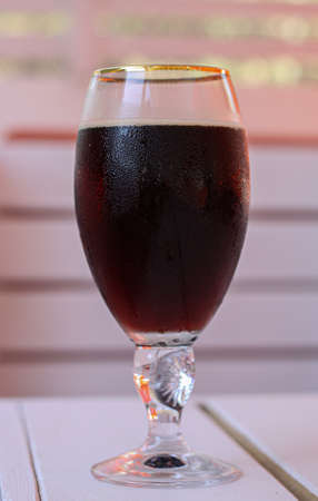 A glass of cold dark beer on a white wooden table in a cafe. The glass is covered with small water droplets. Concept of hot summer thirst quenching, relaxation and fun, drinking beveragesの写真素材