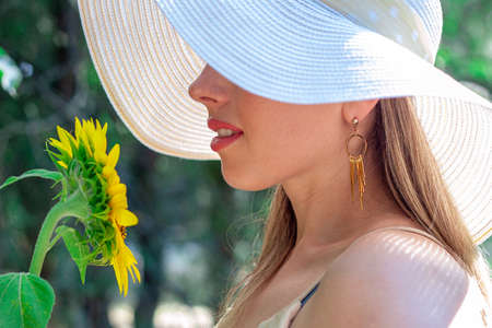 Portrait of one beautiful girl is in the park with a white long flower gladiolus in her hand. The weather is sunny outsideの写真素材