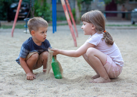 Nikolaev, Ukraine - June 28, 2020: Small boy and girl plays with a sand and green bottleのeditorial素材