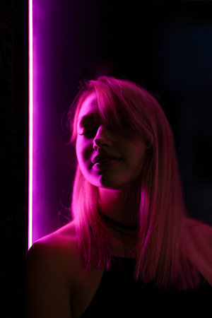 Club style portrait of girl in a black dress. Set is lit with violet light. Picture has dark night...