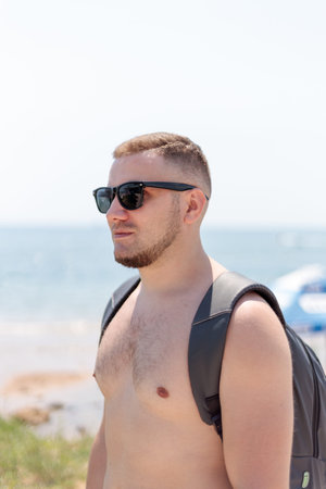 Young stylish man in a black sunglasses walking and relaxing on a beach. Relaxed and cheerful. Outdoor portrait of happy young caucasian man near seaside, Stubble and blacks hair. Summertime.の写真素材