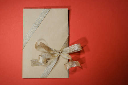 gift envelope with golden ribbons, certificates, invitation inside. Craft concept.Placed on the red background. Copyspace for text. Weddig, ceremony concept, holidays and surprises.の写真素材