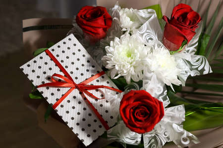 3 red roses bouquet with gift envelope, red ribbons, white paper for certificates, invitation card inside. Craft concept. Red on the red background. Weddig, ceremony concept, holidays, surprises.の写真素材