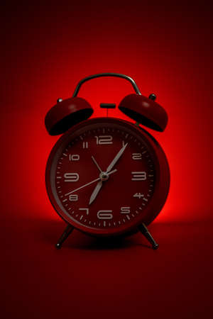 Classic vintage mechanical retro red alarm clock on red background at almost 7 o'clock with copy space. Isolated object. Concept of managing time. Back shadow light, horror atmosphereの写真素材