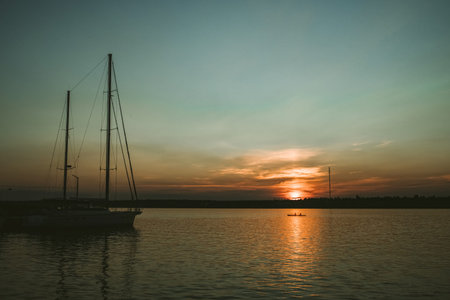Sunset in the river coast side, sun reflects into the water surface. Yachts and boats near the beach