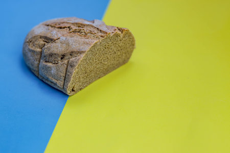 Homemade freshly baked rye and wheat loaf of bread on national Ukrainian flag background,...