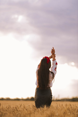 Young girl is standing back in the wheat field wearing Ukrainian national embroidered shirt with...