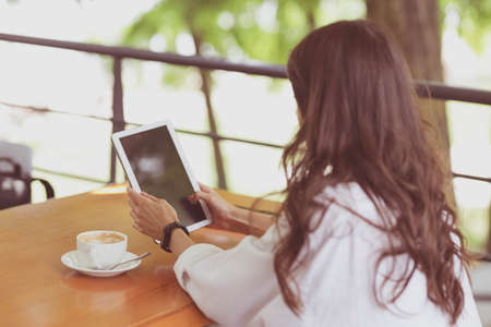 Caucasian lovely young enthusiast blogger girl sitting with digital tablet for designer and cup of coffee during language class in cafe on terrace outside. remote and freelance successful job conceptの写真素材