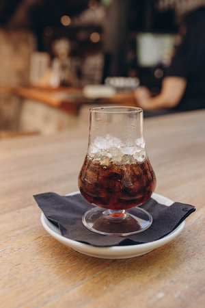 Ice coffee in a tall glass with whiskey. Cold summer drink on a dark napkin and white plate, light...