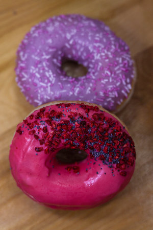 Donuts With Pink and violet Icing And Colored Sprinkles with poppy seeds and dry raspberry on wooden background. Tasty delicious fat high calories sweet food. selective focus. favorite childhood treatの写真素材