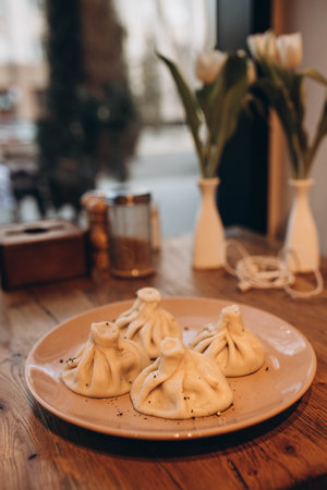 4 Khinkali on the plate in cafe. Blurred bouquet of tender white tulips. Light vintage vase with bunch of flowers is located on the table .の写真素材