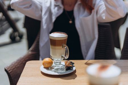 Young female sitting at table in cafe on terrace and drink coffee with sweets after work with sunlight in the afternoon. Rest while travel concept. take a break during a day Spain. Alicanteの写真素材