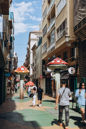 Alicante, Spain - May 16, 2023: People walking funny street Calle de Las Setas (The Mushroom Street) in Alicante old town. Fly agaric (or amanita muscaria) mushrooms creative street design.のeditorial素材