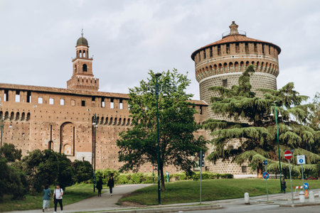 Milan, Italy- May 13, 2023: External view of the corner tower, Castello Sforzesco ancient monument, green lawn of courtyard, blue sky white clouds background,のeditorial素材