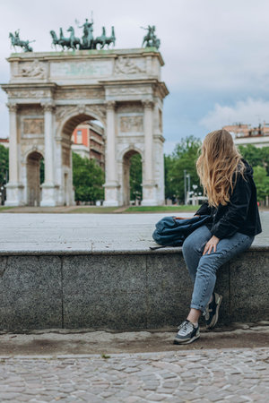 Milan, Italy- May 13, 2023: Girl sits near Arch of Peace or Sempione Gate in Milan, near Sempione Park. Exterior view of the marble gate of the Arco della Sempione, a peace memorial in Milan.の写真素材