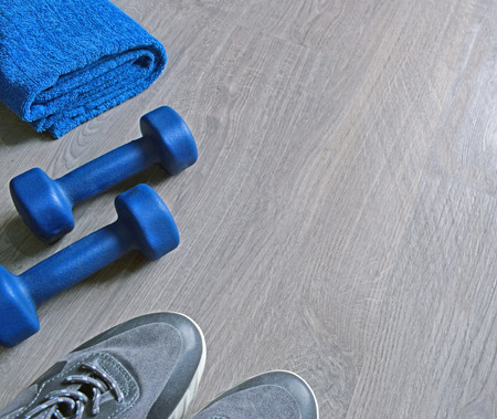 Jeans sneakers, dumbbells and blue towel. Sport fitness objects on light grey wooden background. Active lifestyle, weight loss, body care concept. Empty text space. Top view.の写真素材