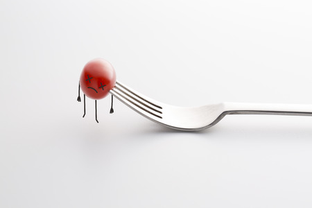 Dead tomato on the fork. Black humor concept photo.の写真素材