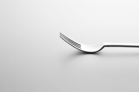 Close-up shot of metallic fork lying down on white surface. Minimalistic design photo.