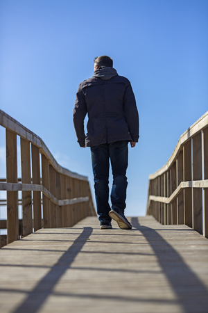 Rear view of a man walking away on wooden boardwalk.の写真素材