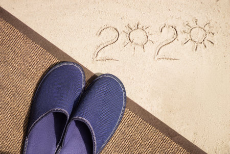 inscription 2020 on yellow sand and slippers