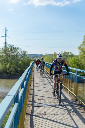 Ivano-Frankivsk, Ukraine - May 3, 2015: tourists on bicycles riding through a pedestrian bridge over the river Bistrica. Bridge railing painted in colors of Ukrainian flag.のeditorial素材