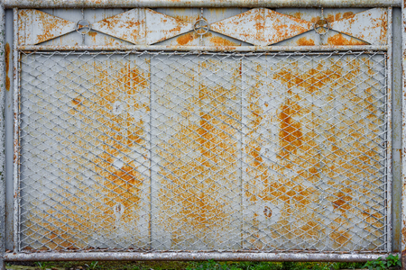 old rusty fence of metal sheets and metal mesh with the remnants of gray paintの写真素材
