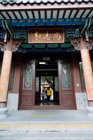 Traditional Chinese Temple Entrance with Wooden Doors, Ornate Carvings, and Visitors Walking Insideの写真素材