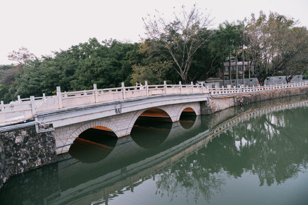 Stone Arch Bridge with Three Arches Over Calm River, Reflective Water, Green Trees, Traditional Architectureの写真素材