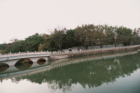 Stone Arch Bridge Over Calm River with Tree Reflections and Autumn Foliageの写真素材