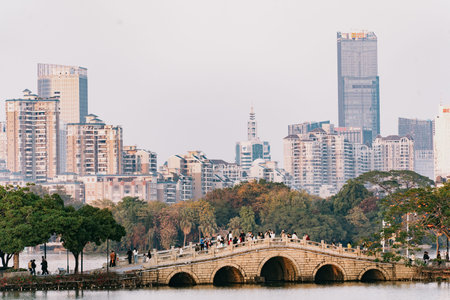 Stone Arch Bridge Over Water with City Skyline and Trees in Backgroundの写真素材