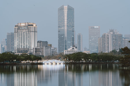 Modern city skyline with glass skyscrapers reflected in calm lake water, urban landscape at duskの写真素材