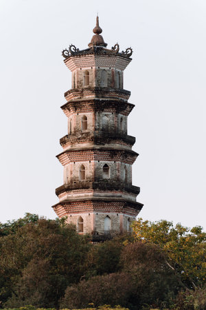 Ancient stone pagoda with multiple tiers standing amidst green trees under overcast skyの写真素材