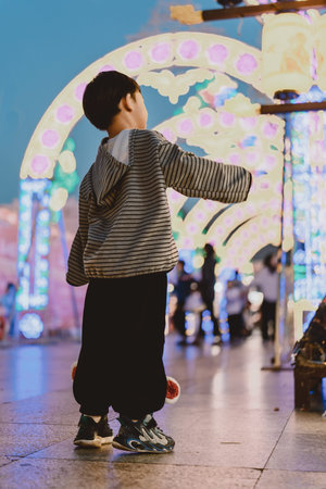 Young boy in striped hoodie walking under glowing archway at night amusement parkの写真素材