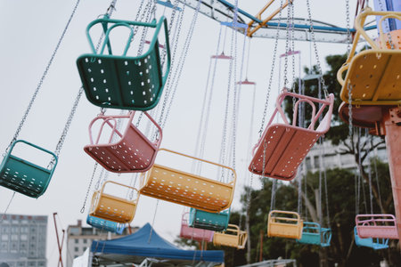 Colorful amusement park swing chairs hanging in mid-air with urban background and overcast skyの写真素材