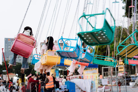 Children riding colorful swing rides at amusement park with urban skyline in backgroundの写真素材