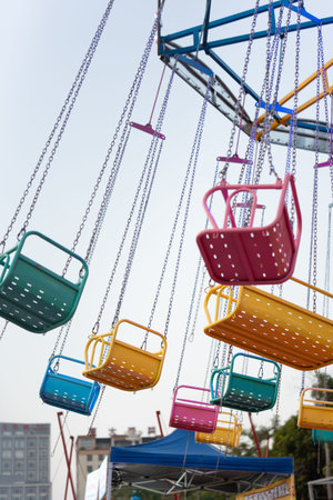 Colorful amusement park swing ride with empty seats hanging from metal frame under cloudy skyの写真素材